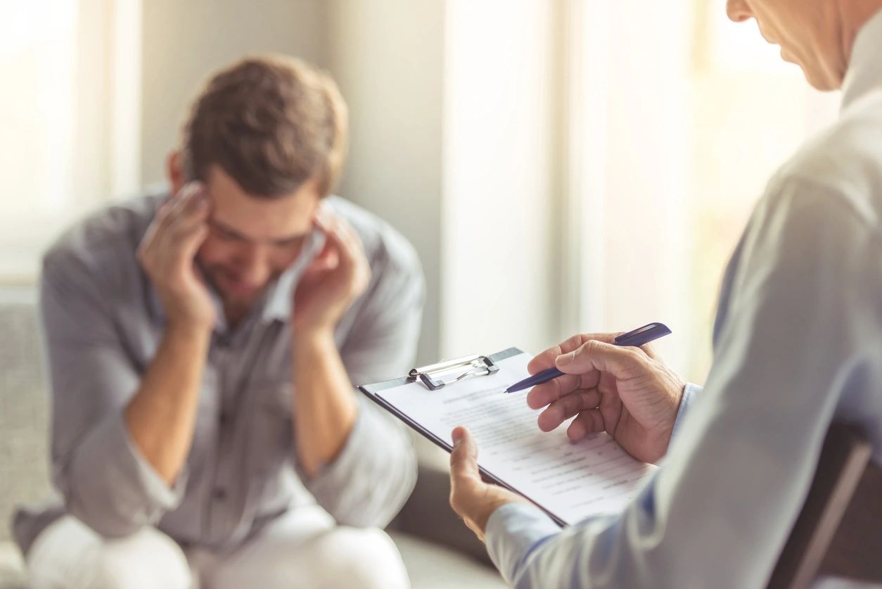 A man holding his head with pain speaking to doctor