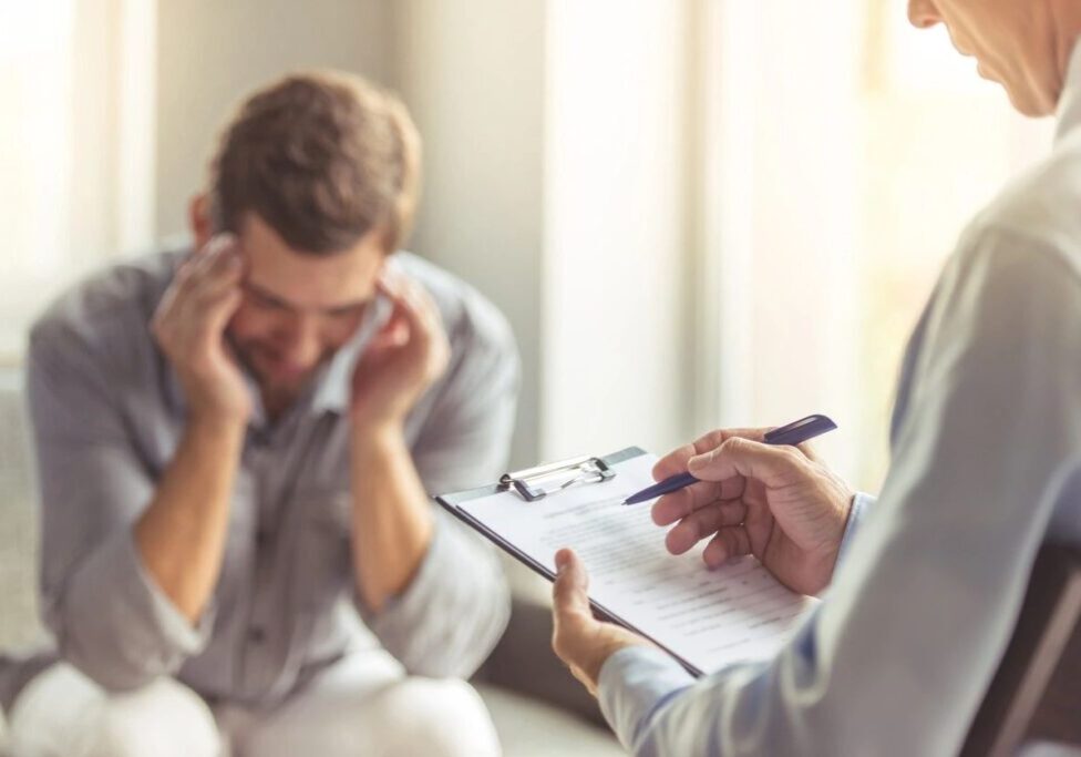 A man holding his head with pain speaking to doctor